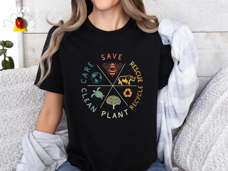 Puede incluir: Camiseta negra con un dise&ntilde;o gr&aacute;fico circular que presenta las palabras "Save, Plant, Clean, Care, Rescue, Recycle" en un estilo vintage. El gr&aacute;fico tambi&eacute;n incluye una abeja, una tortuga, un rinoceronte, un &aacute;rbol y un globo terr&aacute;queo.