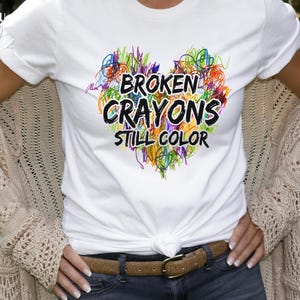 May include: White t-shirt with a colorful heart design and the text "Broken Crayons Still Color".