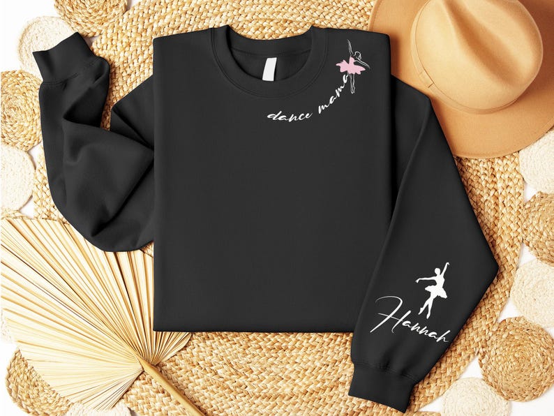 May include: Black sweatshirt with white text that says "dance mama" and a pink ballerina silhouette on the left side. The right sleeve has a white ballerina silhouette and the text "Hannah".
