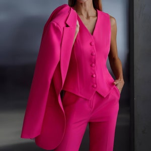 May include: A vibrant fuchsia pink suit, consisting of a tailored blazer draped over the shoulder, a button-down vest, and matching trousers. The suit is a monochromatic ensemble, showcasing a sleek, modern aesthetic. The outfit is a bold fashion statement.