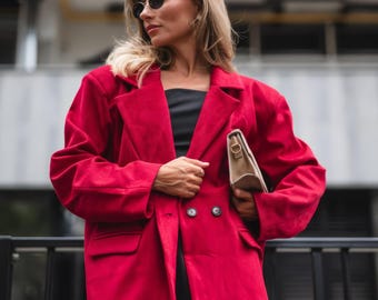 May include: A woman wearing a red blazer with a black dress and a beige handbag. She is wearing sunglasses and has her hair pulled back.