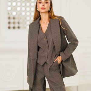 Puede incluir: Un traje gris de tres piezas que consta de una americana, un chaleco y un pantalón de pernera ancha. La americana tiene solapas con muescas y el chaleco tiene cierre de botones. El traje está hecho de una tela texturizada y es adecuado para negocios u ocasiones formales.