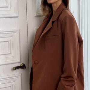 May include: A brown blazer with long sleeves and a single button closure. The blazer has a relaxed fit and a slightly cropped length.