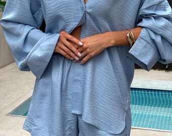 Pode incluir: Um conjunto de camisa e shorts combinando em azul claro. A camisa tem um fecho de botões na frente e os shorts têm um caimento descontraído.