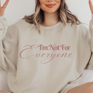 May include: A light beige sweatshirt with the text "I'm Not For Everyone" printed in pink on the front.