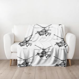 May include: White fleece throw blanket with a black and white print of Apache helicopters. The blanket features multiple helicopters with the word "Apache" printed below each one.