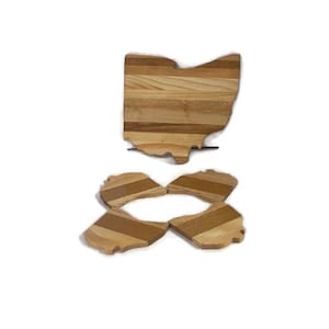 May include: A wooden cutting board shaped like the state of Ohio. The board is made of light and dark wood and has a striped pattern. The board is in two pieces, one large piece and four smaller pieces that fit together to form the shape of the state.