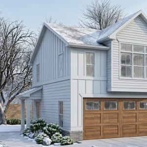Op de afbeelding: Een huis met twee verdiepingen met een lichtblauwe buitenkant, een bruine garagedeur en een met sneeuw bedekt dak. Het huis heeft meerdere ramen en is omgeven door met sneeuw bedekte bomen en struiken. De lucht is lichtblauw.