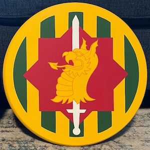 May include: A round wooden plaque with a yellow, green, and red design. The center features a red star with a gold dragon and a white sword. The outer ring is yellow with green stripes.