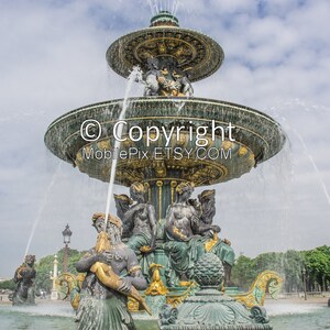 May include: A large, ornate fountain with multiple tiers and sculptures of people and sea creatures. Water sprays from the top of the fountain, creating a misty effect. The fountain is surrounded by trees and a blue sky.
