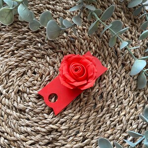 May include: A red rose flower with a red tag attached to it. The rose and tag are on a woven straw surface.