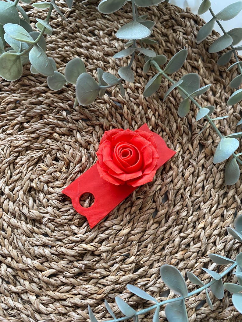 May include: A red rose flower with a red tag attached to it. The rose and tag are on a woven straw surface.