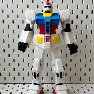 Könnte beinhalten: Ein weißes, blaues, rotes und gelbes Plastikroboter-Spielzeug. Der Roboter hat eine humanoide Form mit Kopf, Armen, Beinen und einem Torso. Der Roboter hat ein schwarzes Visier auf dem Kopf.