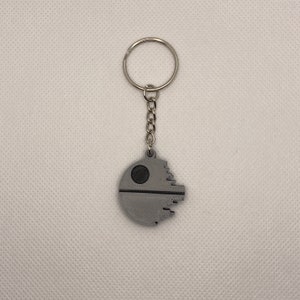 May include: A silver keychain featuring a grey 3D printed Death Star design.
