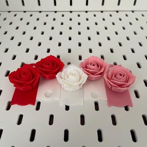 May include: Four artificial roses in different colors: red, pink, white, and a darker pink. The roses are attached to small, scalloped tags in matching colors.