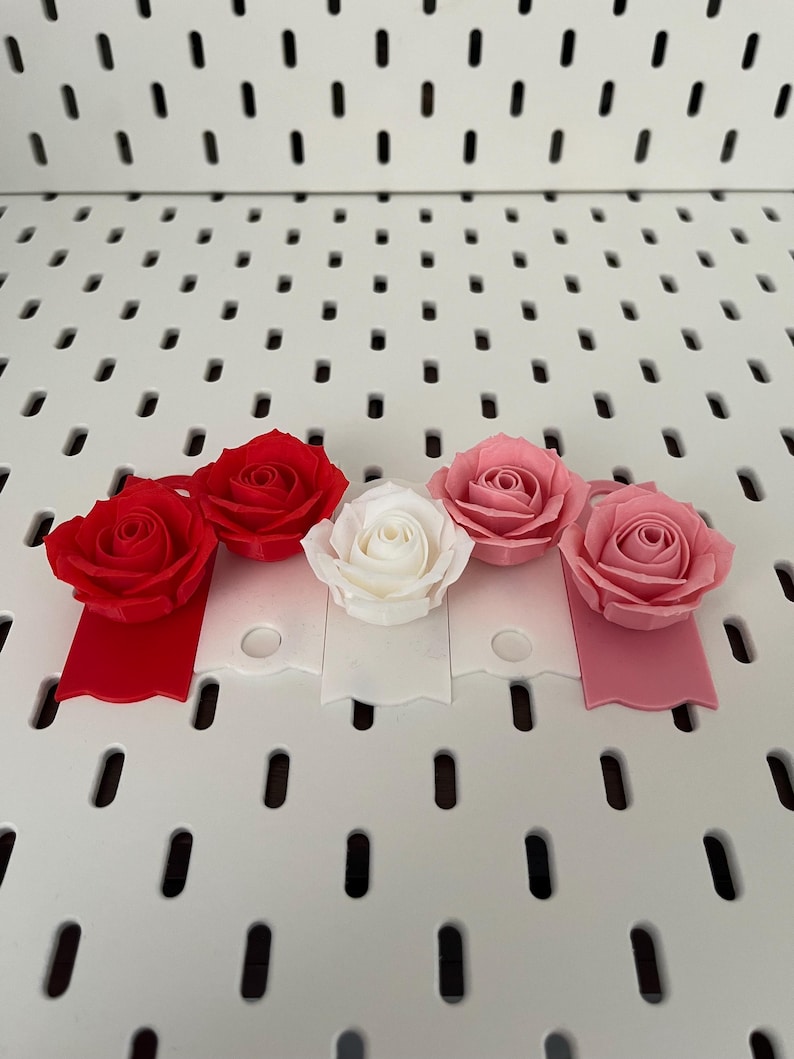 May include: Four artificial roses in different colors: red, pink, white, and a darker pink. The roses are attached to small, scalloped tags in matching colors.