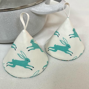 May include: Two white fabric pot holders with teal bunny rabbit designs. The pot holders have a loop handle for easy hanging.