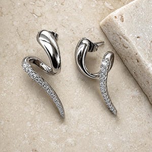 May include: A pair of silver-toned earrings featuring a spiraling, curved design. One side of each earring is smooth and polished, while the other side is encrusted with a row of small, clear, sparkling stones that follow the curve of the metal.