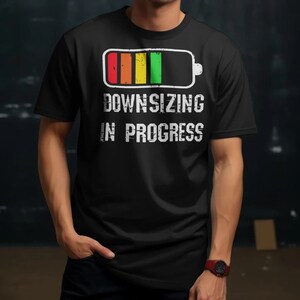 Person wearing a black shirt with the Downsizing in Progress battery design and distressed white text