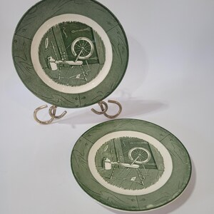 Può includere: Due piatti decorativi verdi e bianchi con un'illustrazione vintage di un filatoio e degli attrezzi. I piatti sono esposti su un supporto in metallo argentato. I piatti hanno un bordo verde con un design strutturato.