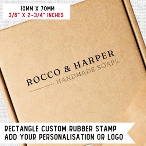 Op de afbeelding: Een bruine kartonnen doos met een zwarte rubberen stempel waarop "ROCCO & HARPER HANDMADE SOAPS" staat. De stempel is rechthoekig en meet 10 mm bij 70 mm. Onder de stempel staat de tekst "RECTANGLE CUSTOM RUBBER STAMP ADD YOUR PERSONALISATION OR LOGO" in zwart.