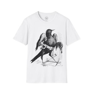 May include: White t-shirt with a black and white illustration of a bird wearing a belt and holding a sword. The illustration is in a vintage style and the text "J. JAQUAUT" is printed below the image.