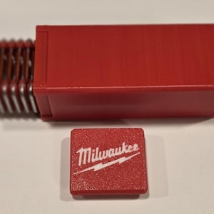 May include: A red plastic case with a stack of metal blades inside. The case has a red lid with the word "Milwaukee" printed in white.