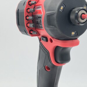 May include: A red and black cordless impact driver with a black grip and a battery pack. The tool has a black head with LED lights and a bit holder with various bits.