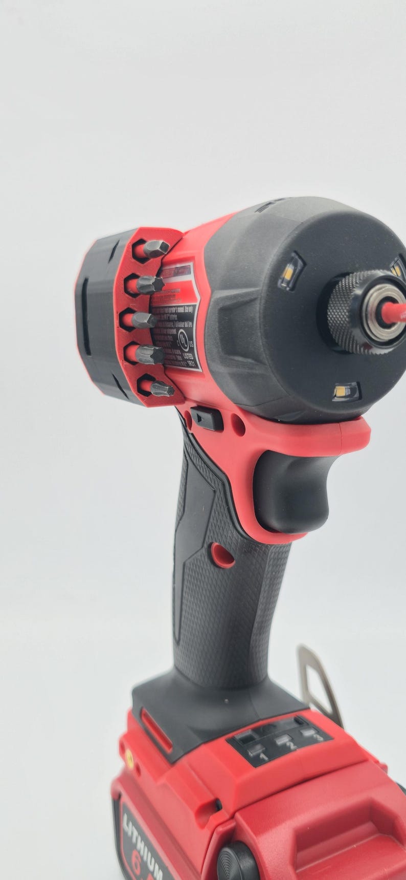May include: A red and black cordless impact driver with a black grip and a battery pack. The tool has a black head with LED lights and a bit holder with various bits.