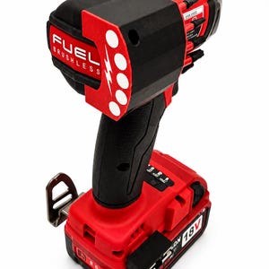 Puede incluir: Un atornillador de impacto inal&aacute;mbrico rojo y negro con el texto "FUEL BRUSHLESS" y un rayo. La herramienta tiene un mango negro y una bater&iacute;a roja de 18 V.