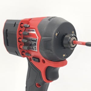 May include: A red and black cordless impact driver with a black grip. The tool has a black head with a red bit inserted. Several bits are stored on the side. The tool is designed for professional use.