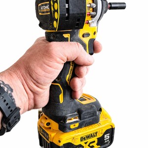 May include: A black and yellow cordless drill with a battery pack. The drill is held in a hand and has the brand name "DEWALT" and "ATOMIC" on it. The drill has a variety of bits attached.