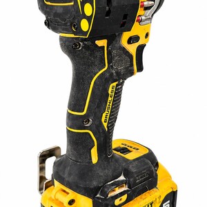 May include: A black and yellow cordless drill with the text "ATOMIC COMPACT SERIES" and "BRUSHLESS". The drill has a black handle with yellow accents and a yellow battery pack. The battery pack reads "DEWALT 20V MAX 5 AH".