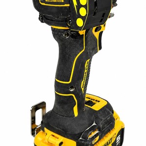 May include: Black and yellow cordless impact driver with the text "ATOMIC COMPACT SERIES" and "BRUSHLESS". The tool has a battery pack that reads "DEWALT 20V".