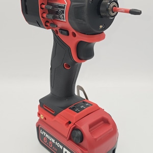 May include: A red and black cordless impact driver with a black handle and a red battery pack. The battery pack is labeled "LITHIUM-ION 6.5 AH 18V". The tool has a black head with a silver bit.