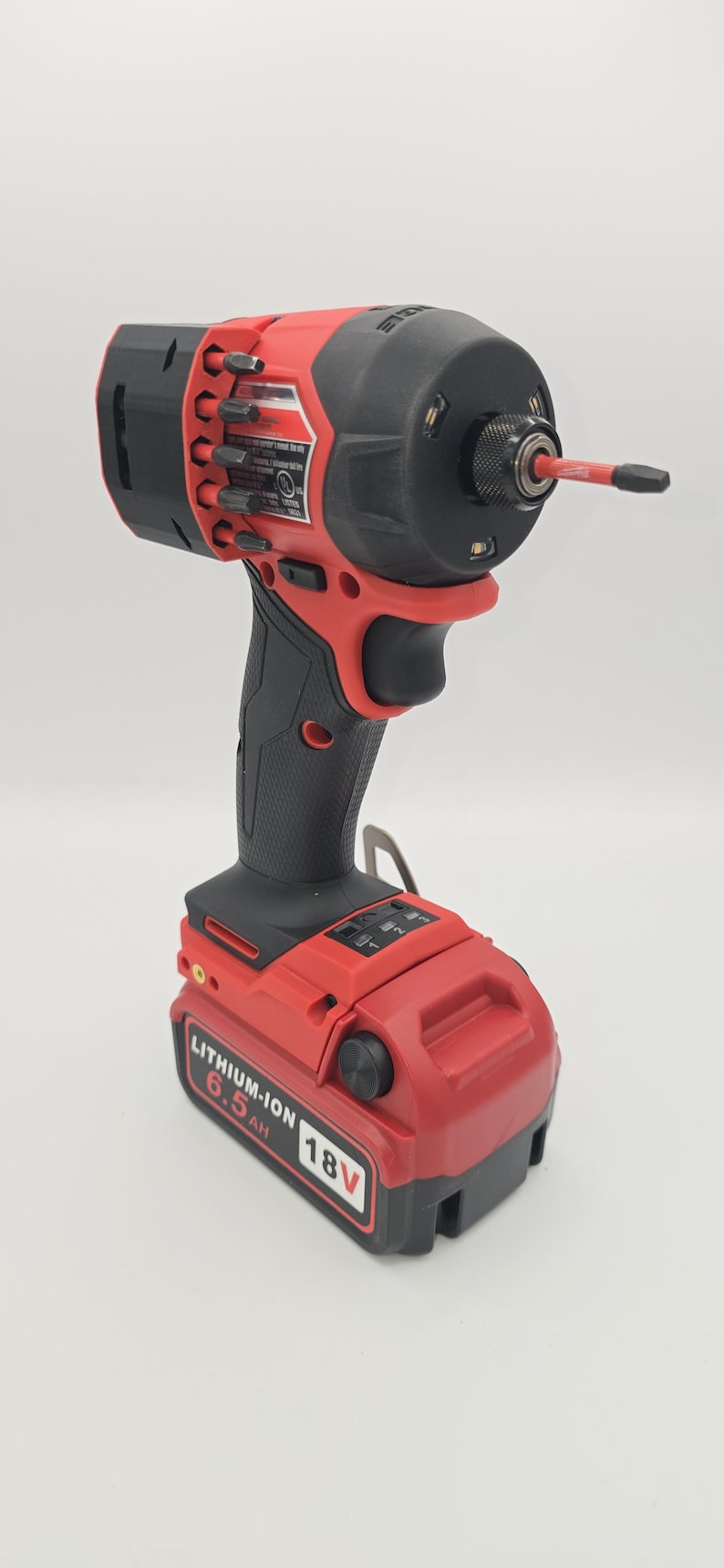 May include: A red and black cordless impact driver with a black handle and a red battery pack. The battery pack is labeled "LITHIUM-ION 6.5 AH 18V". The tool has a black head with a silver bit.