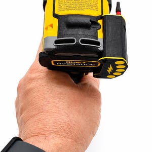 May include: A yellow and black hydraulic tool with the text "QUIET HYDRAULIC" is held in a hand. The tool has a black top and a black side component with a lightning bolt symbol. The tool has a red tip.