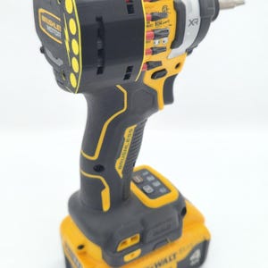 May include: A black and yellow cordless impact driver with a silver head. The tool has the text "BRUSHLESS MOTOR" and "BRUSHLESS" printed on it. The battery reads "20V".