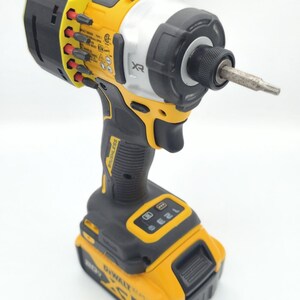 May include: A yellow and black cordless impact driver with a silver head. The tool has a black handle and a battery pack. The brand name "DeWalt" is visible on the battery. A bit is inserted in the front.