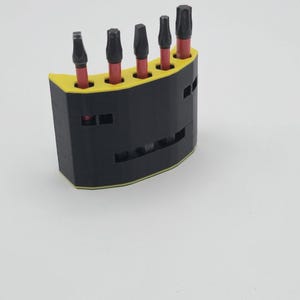 May include: A black and yellow tool holder with five black and red bits. The holder is semi-circular with a yellow top and a black base. The bits are arranged in a row, each with a black head and a red shaft.