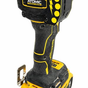 May include: Black and yellow cordless impact driver with the text "ATOMIC COMPACT SERIES" and "BRUSHLESS". The tool has a battery pack that reads "DEWALT 20V".