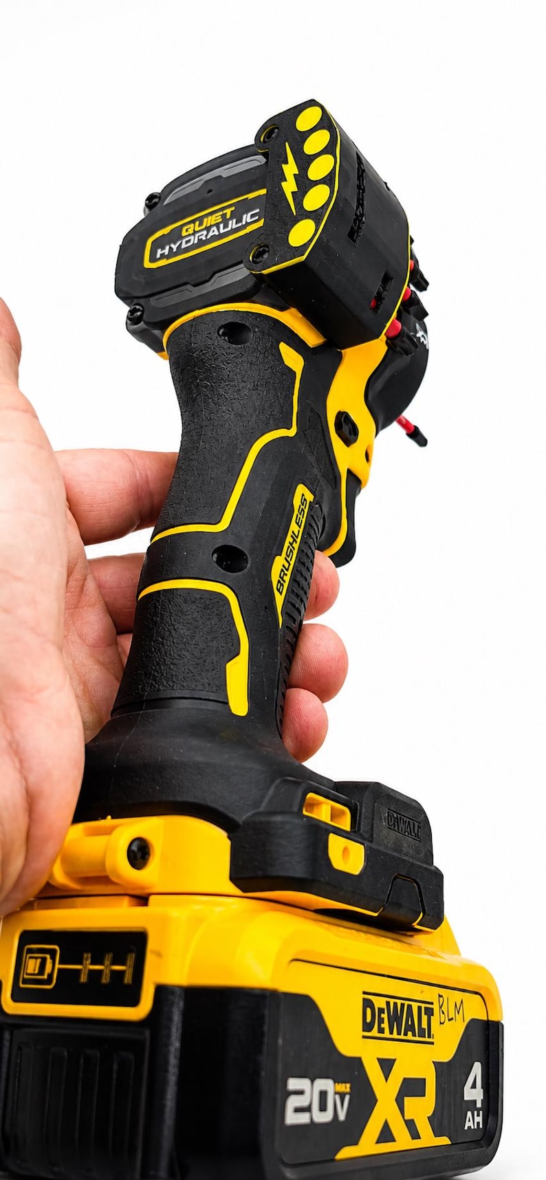 May include: Black and yellow cordless drill with the text "QUIET HYDRAULIC" and "BRUSHLESS". The drill has a black handle with yellow accents and a yellow battery pack with "DEWALT" and "20V" printed on it.