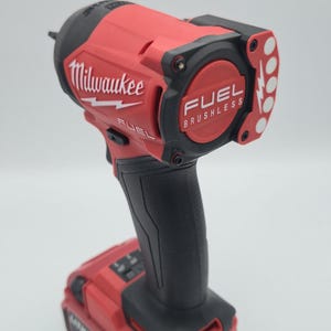 May include: A red and black Milwaukee FUEL brushless impact wrench. The tool features the Milwaukee logo and the text "FUEL BRUSHLESS". The impact wrench has a black handle and a battery pack attached.