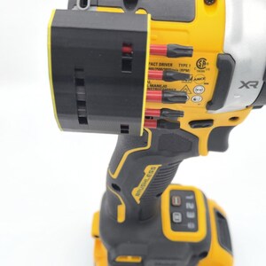 May include: A yellow and black cordless impact driver with a black bit holder attached. The driver has the brand name "DEWALT" and "BRUSHLESS" printed on it. The bit holder contains several black and red bits.