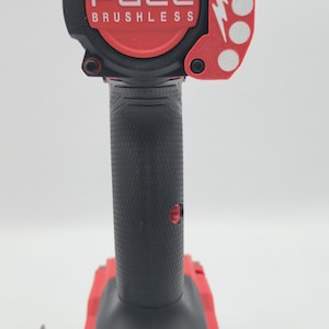 May include: Red and black FUEL brushless impact wrench. The tool has a black handle with a textured grip and a red base. The head of the tool is red with the word FUEL and the word BRUSHLESS in white.