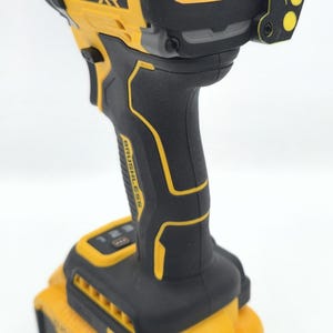 May include: A yellow and black DeWalt 20V XR brushless motor impact driver. The tool has a black handle with yellow accents and a yellow battery pack. The text "DEWALT" and "BRUSHLESS MOTOR" are visible on the tool.