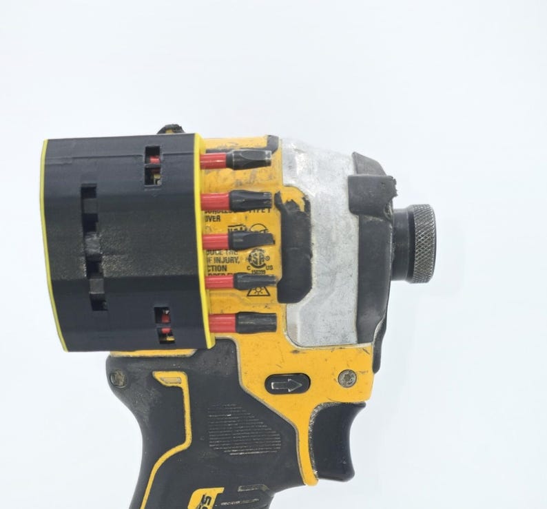 May include: A yellow and black cordless impact driver with a black head. The tool has a silver metal body and a black handle. The impact driver has the text "Reduce the risk of injury" printed on it.