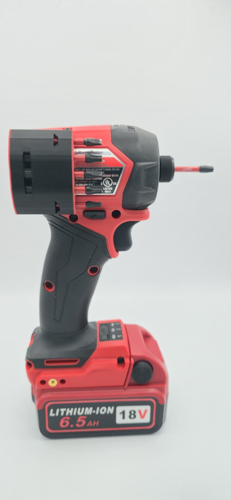 May include: A red and black cordless impact driver with a black handle and a red battery pack. The battery pack is labeled "LITHIUM-ION 6.5AH 18V". The tool has a black chuck and a red bit.