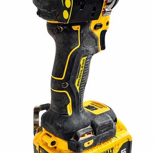 May include: A black and yellow cordless drill with the text "ATOMIC COMPACT SERIES" and "BRUSHLESS". The drill has a 20V battery with the text "DEWALT" and "5 AH".