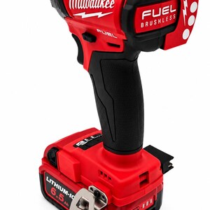 Puede incluir: Atornillador de impacto inal&aacute;mbrico rojo y negro con el logotipo "Milwaukee". La herramienta tiene un mango negro y una bater&iacute;a roja con la etiqueta "LITHIUM-ION 6.5 Ah". Las palabras "FUEL BRUSHLESS" tambi&eacute;n est&aacute;n impresas.
